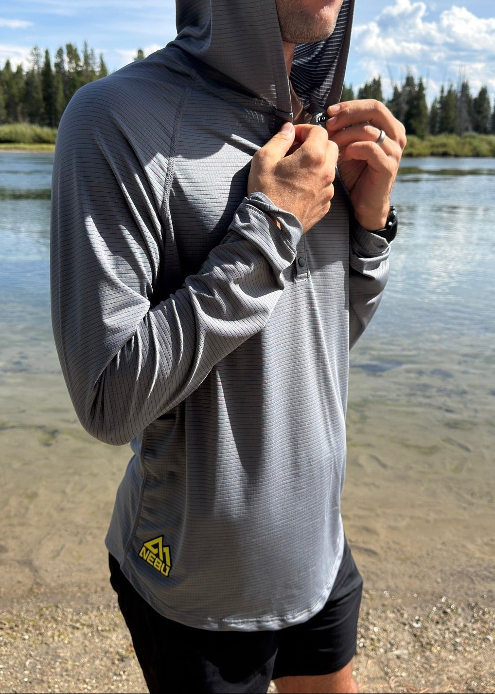 Man wearing the Nebu Gimlet Sun Hoodie, hood up, beside a river in Yellowstone